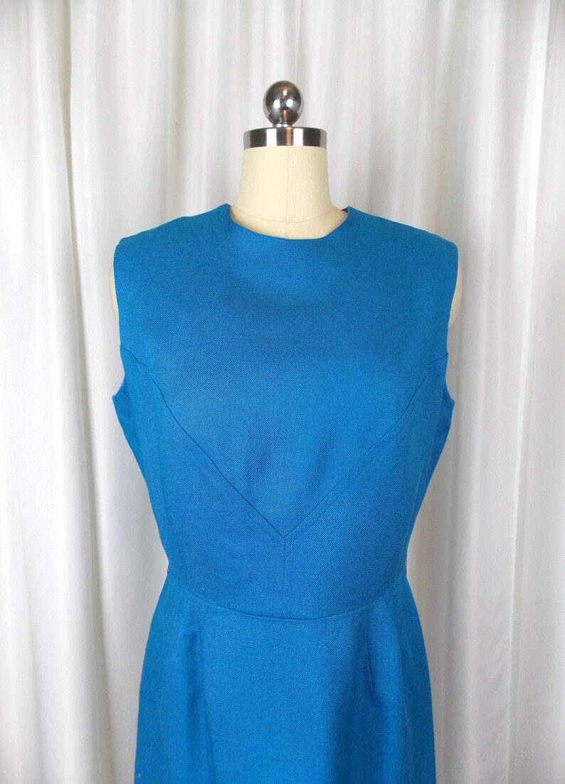 May include: A sleeveless, knee-length dress in a vibrant blue hue. The dress features a classic, tailored silhouette with a scoop neckline and a subtle V-shaped detail at the bodice. The fabric appears to have a textured weave.