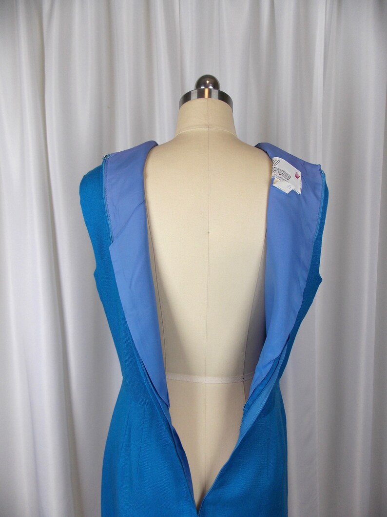 May include: A sleeveless, turquoise blue dress with a light blue lining, displayed on a mannequin. The dress has a visible zipper down the back. A tag with the name "Rothschild" is visible on the inside of the dress.