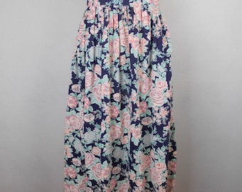 May include: A long, navy blue skirt with a floral print featuring pink and white roses. The skirt has a gathered waist and a flowing silhouette.