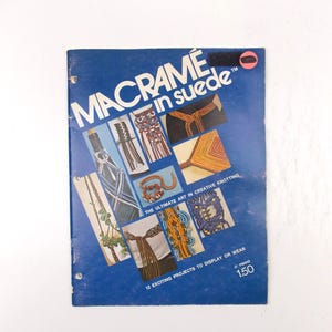 May include: A vintage book titled "Macramé in Suede" with a blue cover. The cover features various macramé projects in different colors and designs. The text includes "The Ultimate Art in Creative Knotting" and "12 Exciting Projects to Display or Wear".