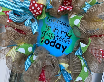May include: A brown burlap wreath decorated with blue, green, red, and yellow striped and polka dot ribbon. The wreath has a blue circle in the center with the text "The future of the world is in my classroom today".