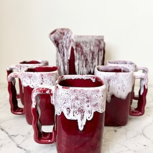 Puede incluir: Juego de seis tazas de cerámica roja y blanca con cuerpos cuadrados y un efecto de glaseado en goteo. Las tazas tienen un diseño único y texturizado y son perfectas para servir café, té u otras bebidas.