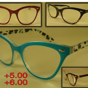May include: Four pairs of cat-eye reading glasses with different colored frames and patterns. The frames are red, black, blue with a white and black pattern, and pink. The lenses are clear. The text +5.00 and +6.00 is visible in the image.
