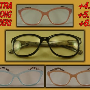 May include: Three pairs of reading glasses with black, pink, and blue frames. The glasses are labeled "EXTRA STRONG READERS". The text +4.00, +5.00, and +6.00 is visible in the image.