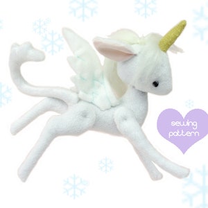 May include: A white plush unicorn sewing pattern with a gold horn, white wings, and a long tail. The pattern is on a white background with snowflakes.