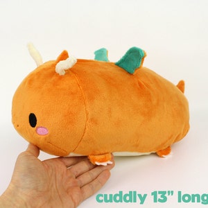 May include: A plush orange dragon with a green fin and white horns. It is 13 inches long and has a cute embroidered face.