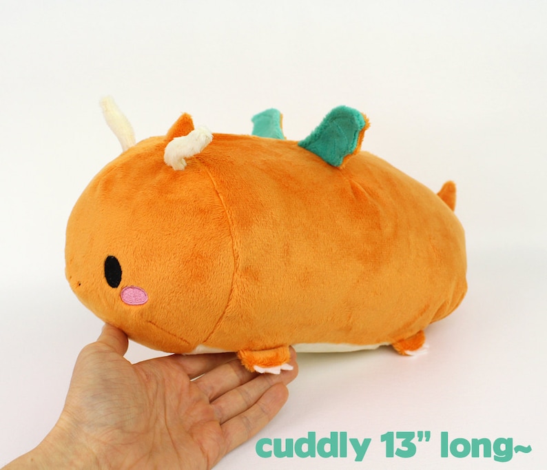 May include: A plush orange dragon with a green fin and white horns. It is 13 inches long and has a cute embroidered face.