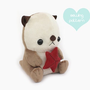 May include: A plush toy otter with brown fur and a white belly. The otter is holding a red starfish in its paws. The toy is sitting on a white background.  The text "sewing pattern" is in a blue heart shape above the toy.