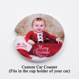May include: A round white car coaster with a photo of a baby in a Santa suit sitting in a red stocking. The text "My First Christmas" and "Merry Christmas" is printed on the coaster.