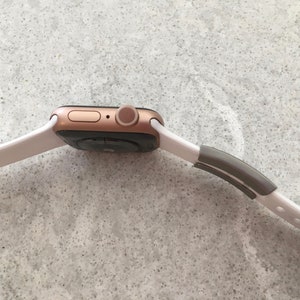 May include: A rose gold Apple Watch with a white sport band and a grey sport loop.