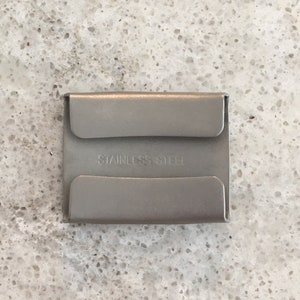 May include: A silver metal card holder with the words "Stainless Steel" printed on the front.