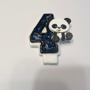 May include: A blue and black candle shaped like the number four with a white panda bear holding a green bamboo shoot on the side.