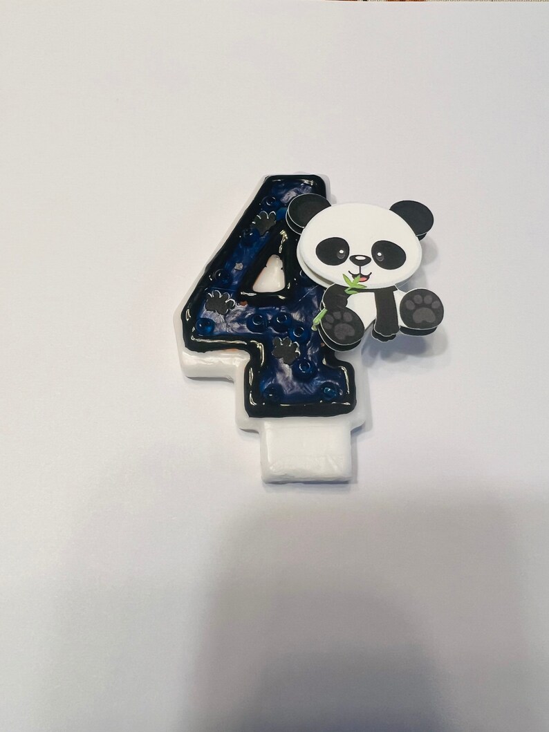 May include: A blue and black candle shaped like the number four with a white panda bear holding a green bamboo shoot on the side.