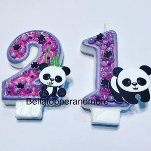 May include: Two purple and pink birthday candles with panda bears. The candles are shaped like the numbers 2 and 1. The panda bears are black and white and have a cute expression.