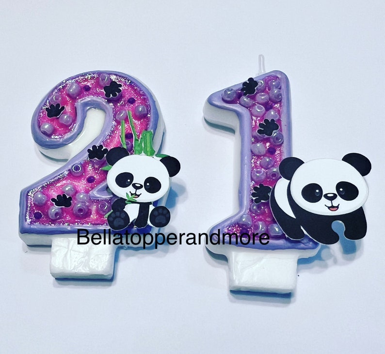 May include: Two purple and pink birthday candles with panda bears. The candles are shaped like the numbers 2 and 1. The panda bears are black and white and have a cute expression.