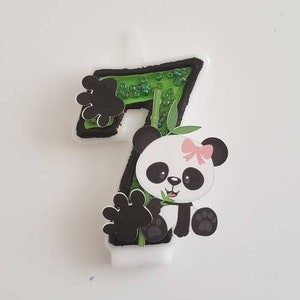 May include: A green and black number seven candle with a panda bear holding a piece of bamboo. The panda has a pink bow on its head.