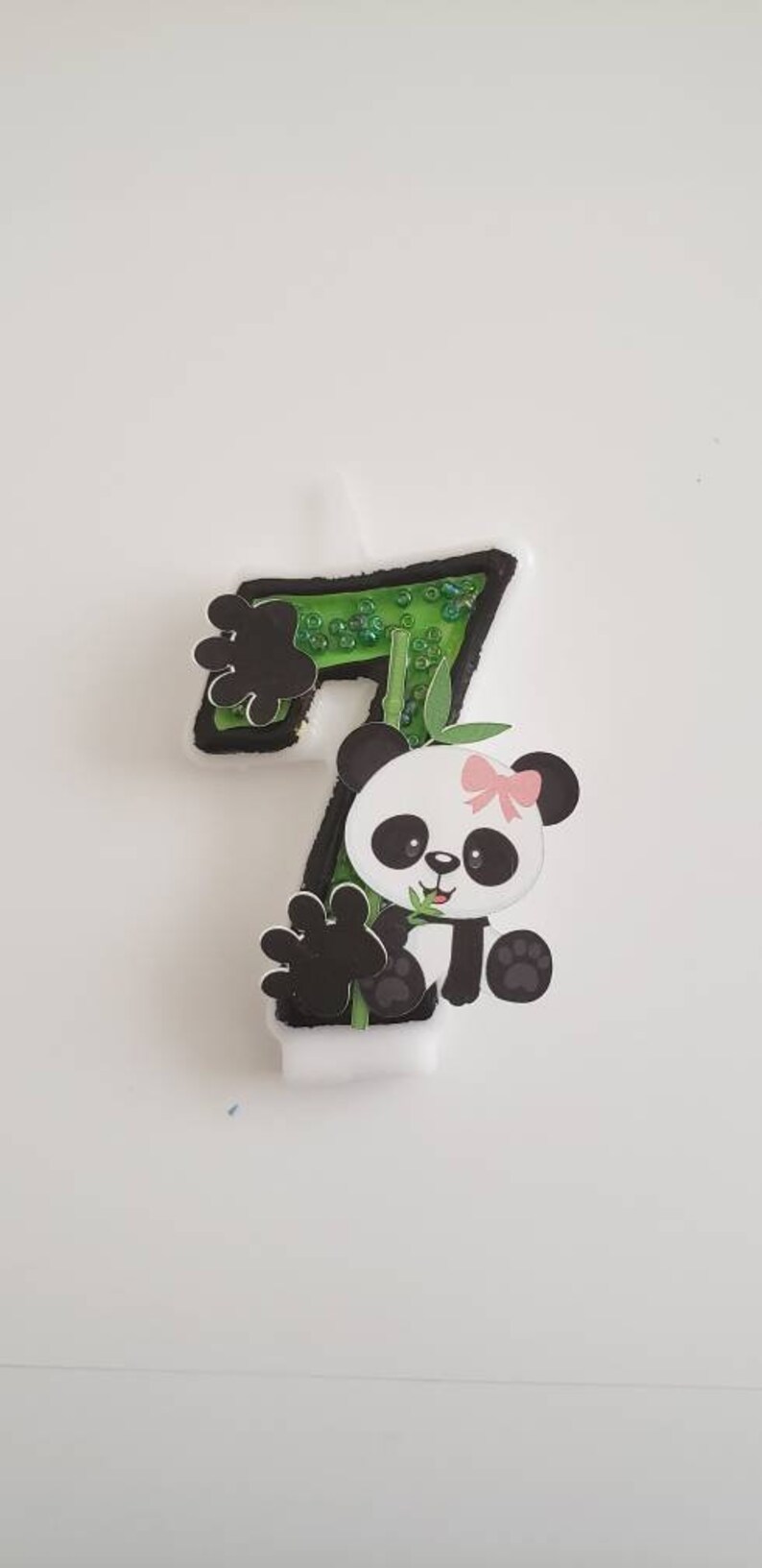 May include: A green and black number seven candle with a panda bear holding a piece of bamboo. The panda has a pink bow on its head.