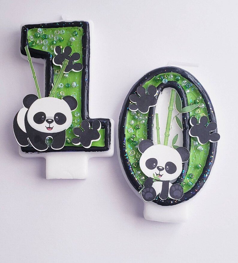 May include: Two green and black panda birthday candles, one shaped like the number 1 and the other shaped like the number 0. Each candle has a panda bear with black eyes and a bamboo stalk.