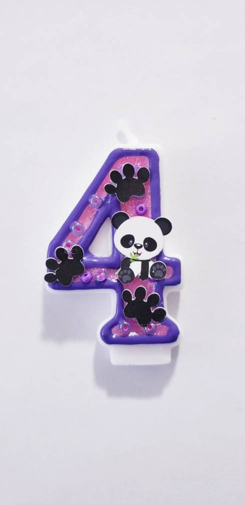 May include: Purple and pink number four birthday candle with a panda bear design. The candle has glitter and paw prints.