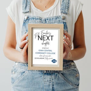 May include: A framed print with the text "Emilee's NEXT chapter" in black script. The print also includes the text "STARTS AT IOWA CENTRAL COMMUNITY COLLEGE" and a college logo. The frame is a light wood color.