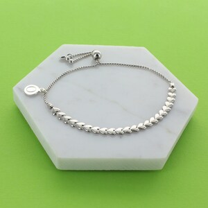 May include: A silver heart charm bracelet with an adjustable sliding clasp. The bracelet is made of a chain of small, connected heart-shaped links.