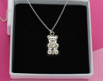 May include: A silver necklace with a small, detailed bear pendant. The necklace is displayed in a white box with a black interior.
