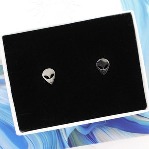 May include: A pair of silver alien head stud earrings in a black velvet jewelry box.