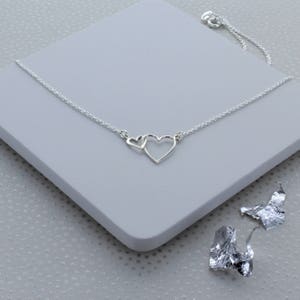 May include: A silver necklace with a delicate chain and two interlocking heart pendants. The hearts are open and connected at the top.