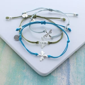 May include: Three adjustable bracelets with silver bee charms. The bracelets are made with turquoise, light blue, and olive green cord.