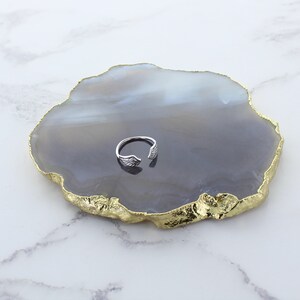 Puede incluir: Anillo de plata con dise&ntilde;o de ala sobre un posavasos de &aacute;gata gris y dorado.