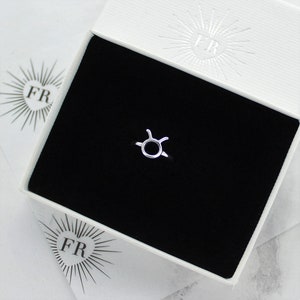 May include: A silver ring with a Taurus zodiac symbol design. The ring is displayed in a white box with the letters "FR" on the lid.