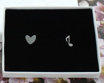 May include: A pair of silver stud earrings in a black velvet box. One earring is a heart shape and the other is a music note.