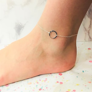 以下が含まれることがあります： 小さなビーズでできた繊細な円形のチャームが付いたシルバー製のアンクレット。円形のチャームは滑らかで磨かれた仕上げになっています。