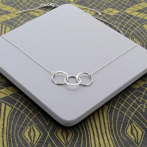 May include: A silver necklace with three interlocking circles. The necklace is on a grey surface.