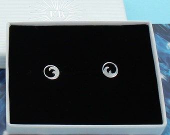 May include: A pair of silver wave earrings in a black velvet jewelry box. The earrings are small and delicate, with a simple design.