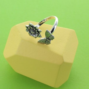 May include: Silver ring featuring a sunflower and butterfly design. The ring is open and adjustable.
