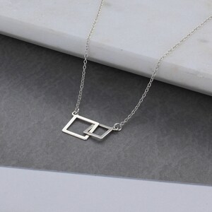 May include: A silver chain necklace with a pendant featuring two interlocking square shapes.
