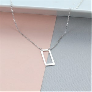 May include: A silver chain necklace with a rectangular pendant. The pendant has a cut-out design in the shape of a triangle.