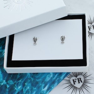 May include: A pair of silver lobster earrings in a white box with a black interior. The earrings are small and delicate, and they are perfect for adding a touch of whimsy to any outfit.