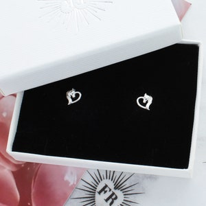 May include: A pair of silver horse head stud earrings in a white box with black velvet lining. The horse head is in a heart shape.