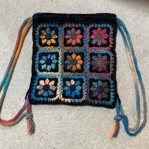 May include: A crocheted drawstring bag with a black background and colorful floral patterns. The bag has two long, colorful straps.