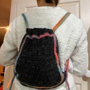 May include: A black crocheted backpack with colorful stripes. The straps are made of the same colorful yarn.
