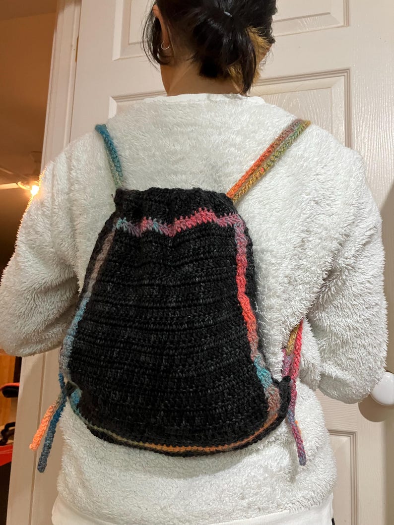 May include: A black crocheted backpack with colorful stripes. The straps are made of the same colorful yarn.