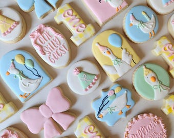 May include: Assortment of decorated sugar cookies in various shapes, including bows, the number "one", and circles. The cookies feature pastel colors, goose designs with party hats and balloons, and the text "One Silly Goose".