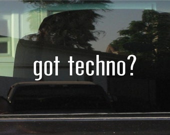 May include: Image of a car window with the text "got techno?" in white, bold letters. The background shows a blurred view of a house and trees, with reflections on the glass.