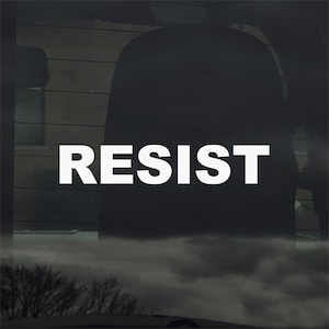 Op de afbeelding: Witte vinyl sticker met het woord "RESIST" in een vetgedrukte, schreefloze lettertype. De sticker is aangebracht op een autoruit, met een donker interieur en een bewolkte lucht zichtbaar door het glas. De algehele esthetiek is eenvoudig en direct.
