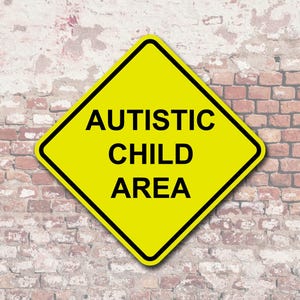 May include: A yellow diamond-shaped sign with black text that reads "AUTISTIC CHILD AREA." The sign has a black border and is set against a brick wall background.