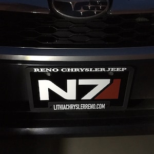 May include: A black number plate with white text that reads "RENO CHRYSLER JEEP" and "LITHIACHRYSLERRENO.COM". The plate has a white and red logo that reads "N71".