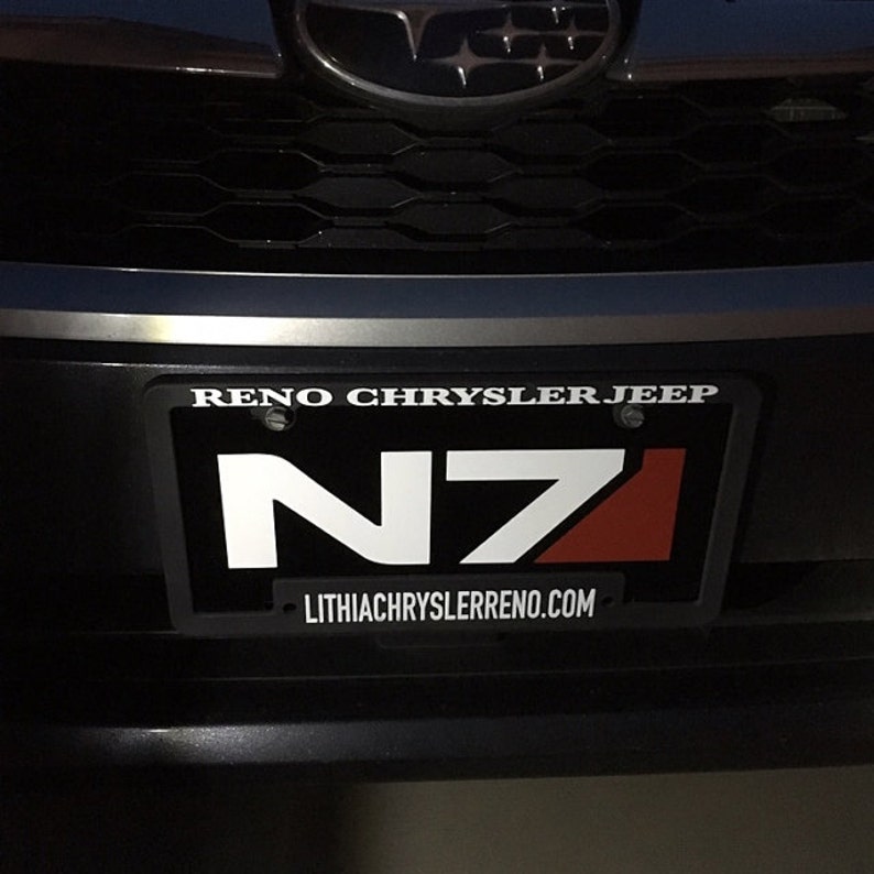 May include: A black number plate with white text that reads "RENO CHRYSLER JEEP" and "LITHIACHRYSLERRENO.COM". The plate has a white and red logo that reads "N71".