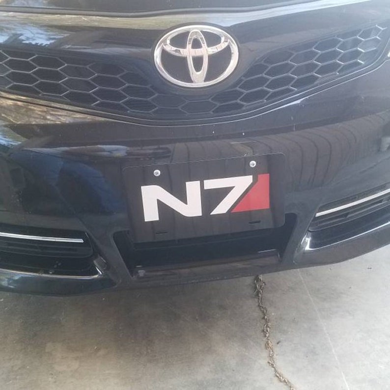 May include: A black car with a silver Toyota emblem on the front grille. The car has a number plate that says "N7" in white letters on a black background with a red accent.